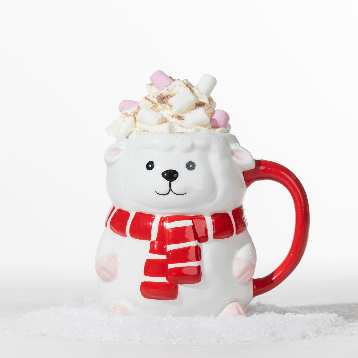 Christmas sheep mug with a red striped scarf, filled with whipped cream and pink and white marshmallows in a snowy festive setting.