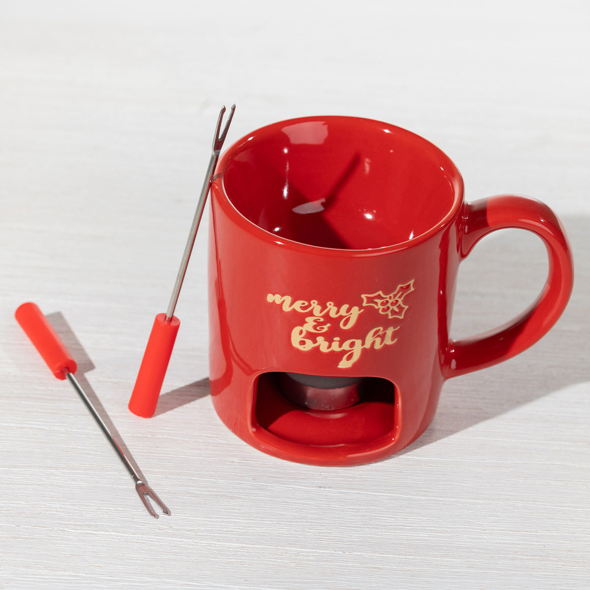 Red Christmas fondue mug with two red-handled fondue forks, featuring gold “Merry & Bright” detailing and a compartment for a tealight candle.