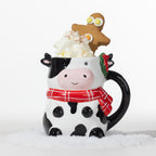 Christmas cow mug with black spots, a red tartan scarf and holly detail, topped with whipped cream and a gingerbread man.