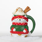 Christmas cat mug in green with red and white festive details, topped with whipped cream and cinnamon sticks.
