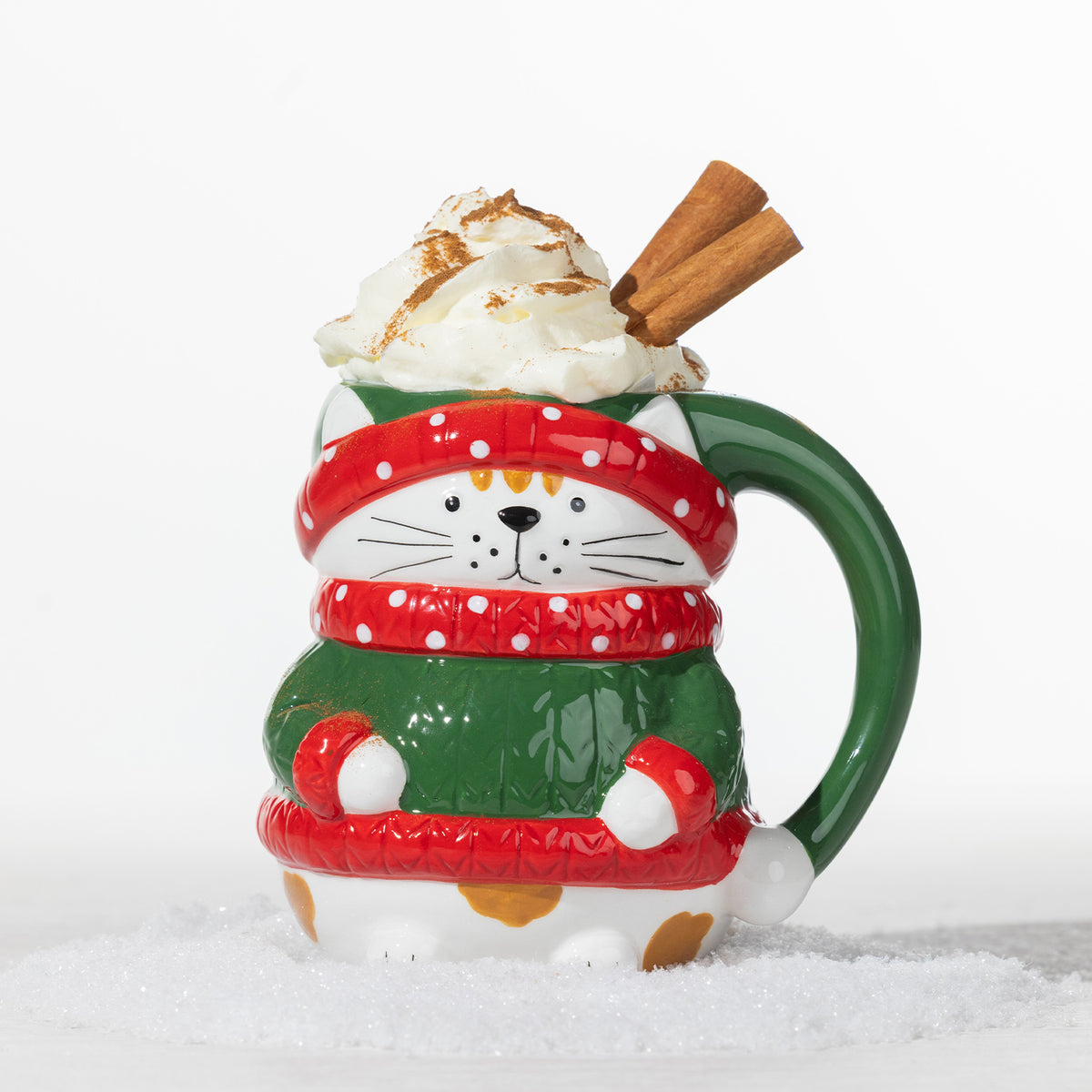 Christmas cat mug in green with red and white festive details, topped with whipped cream and cinnamon sticks.