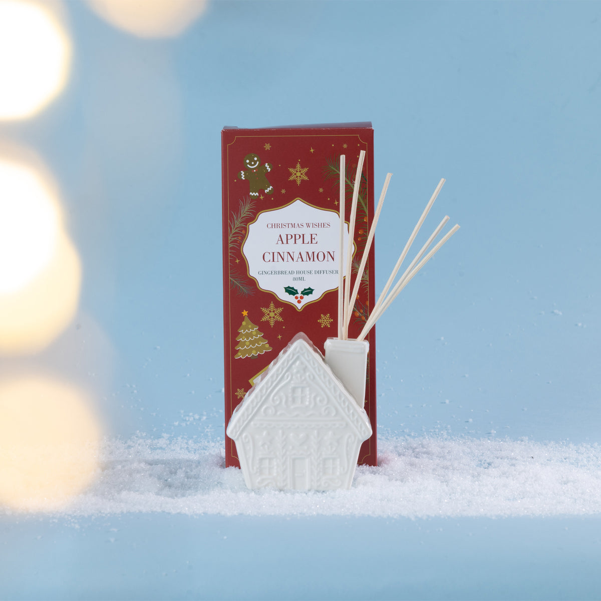 A festive Apple Cinnamon diffuser featuring a charming white gingerbread house vessel, styled in a snowy setting with soft glowing lights.