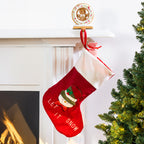 A red Christmas stocking with a white cuff hangs from a mantel. The stocking features an embroidered snowman and the words 'LET IT SNOW'.