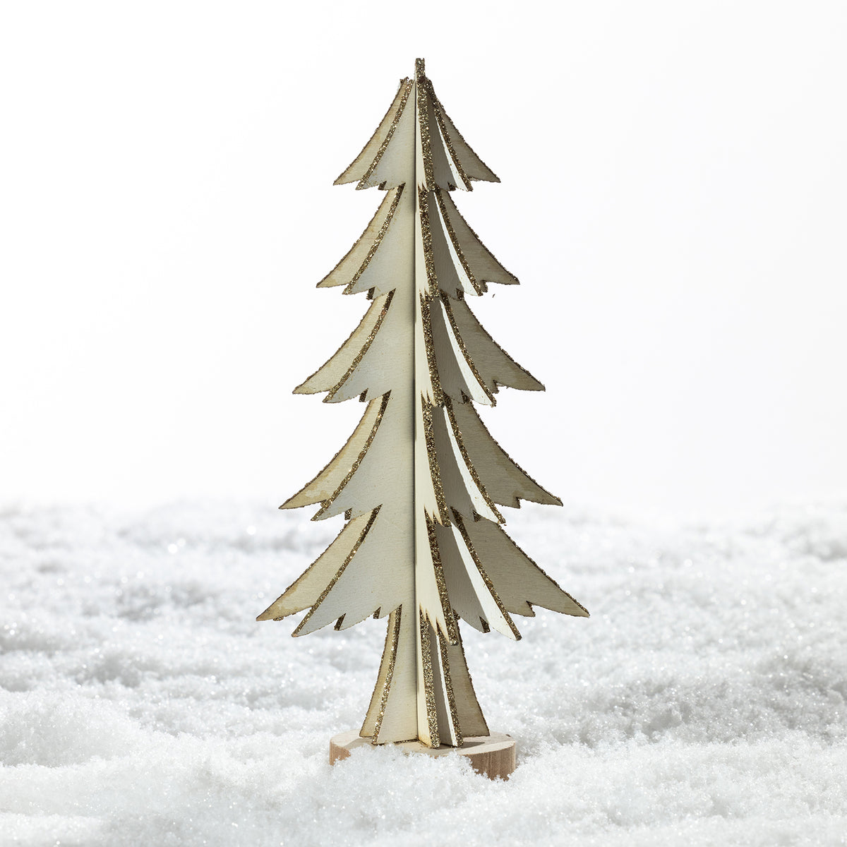 A small decorative wooden Christmas tree stand made of layered light wood, standing upright in white faux snow against a bright white background.