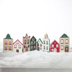 A row of colorful miniature house cutouts arranged on a white snowy surface against a plain white background.