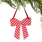 A red and white striped bow-shaped Christmas ornament hanging from a green pine branch against a white background.