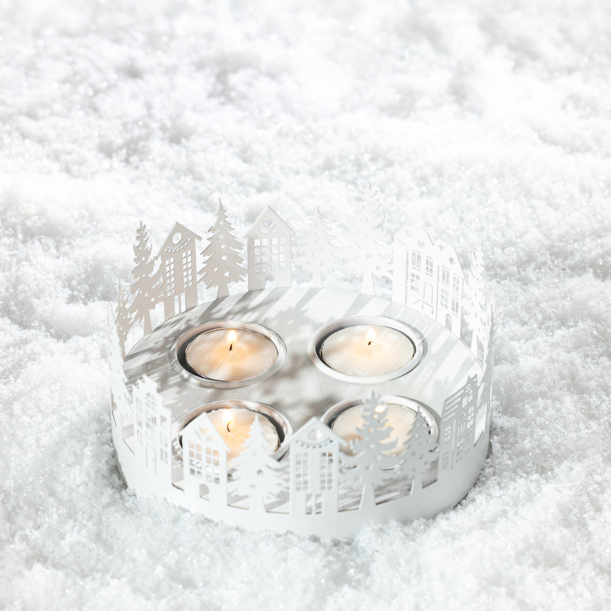 Christmas Wishes Metal Village Candle Holder – White metal candle holder with intricate cut-out houses and Christmas trees surrounding four tealight candle spaces.