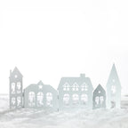 Christmas Wishes Metal Village Screen – White metal folding Christmas village screen featuring cut-out houses, windows, stars, trees and reindeer scenes.