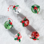 Six decorative jingle bells arranged on a white snowy surface. The bells are white, green, and red, each decorated with red berries, green holly leaves, white snowflakes, and black star cutouts, with red-and-white striped hanging ribbons.