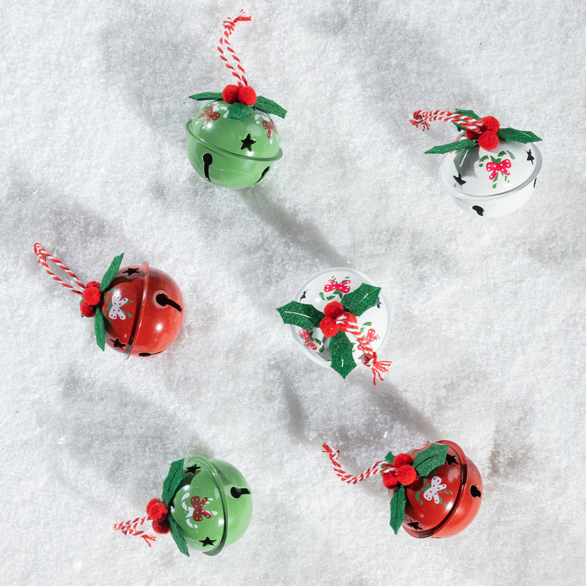 Six hand-painted Christmas jingle bells in red, green, and white, decorated with holly leaves, candy canes, and red berries, arranged on a white snowy background.