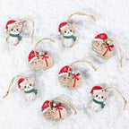 Eight wooden Christmas ornaments shaped like cute kittens, each wearing a red Santa hat and scarf, arranged on a white textured background.