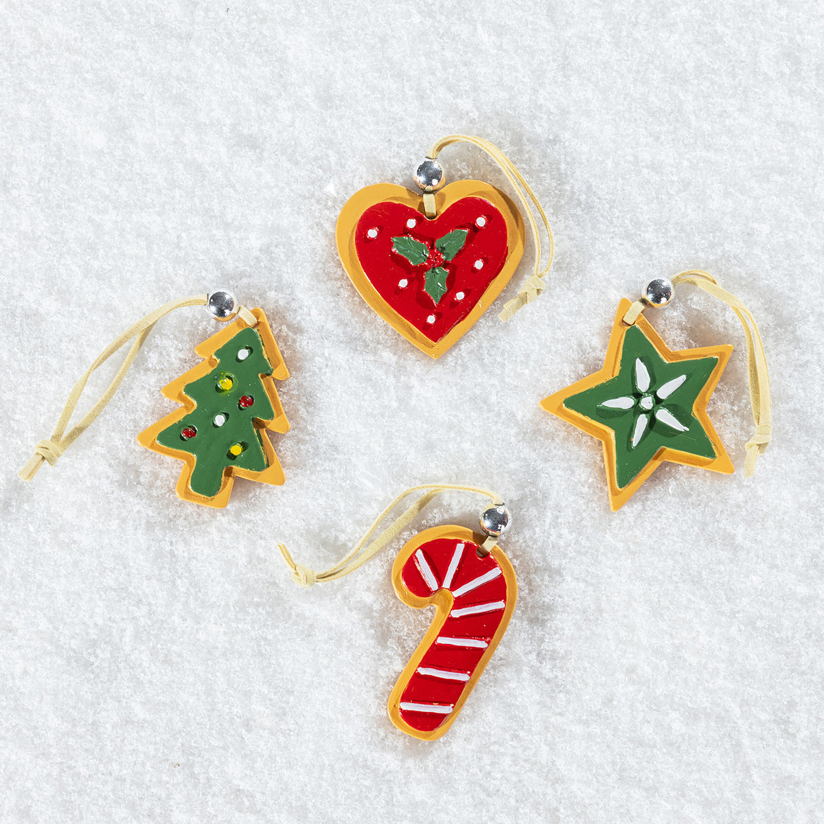 Four Christmas tree-shaped ornaments in different designs, including a red heart with green holly, a green Christmas tree with ornaments, a green star with a white flower, and a red and white striped candy cane, all with gold hanging loops, displayed on a white textured background.