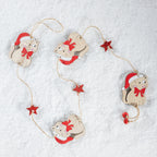 A Christmas garland featuring four wooden cat ornaments wearing red Santa hats and red bows, connected by a string with small red star accents, laid out on a white textured surface.