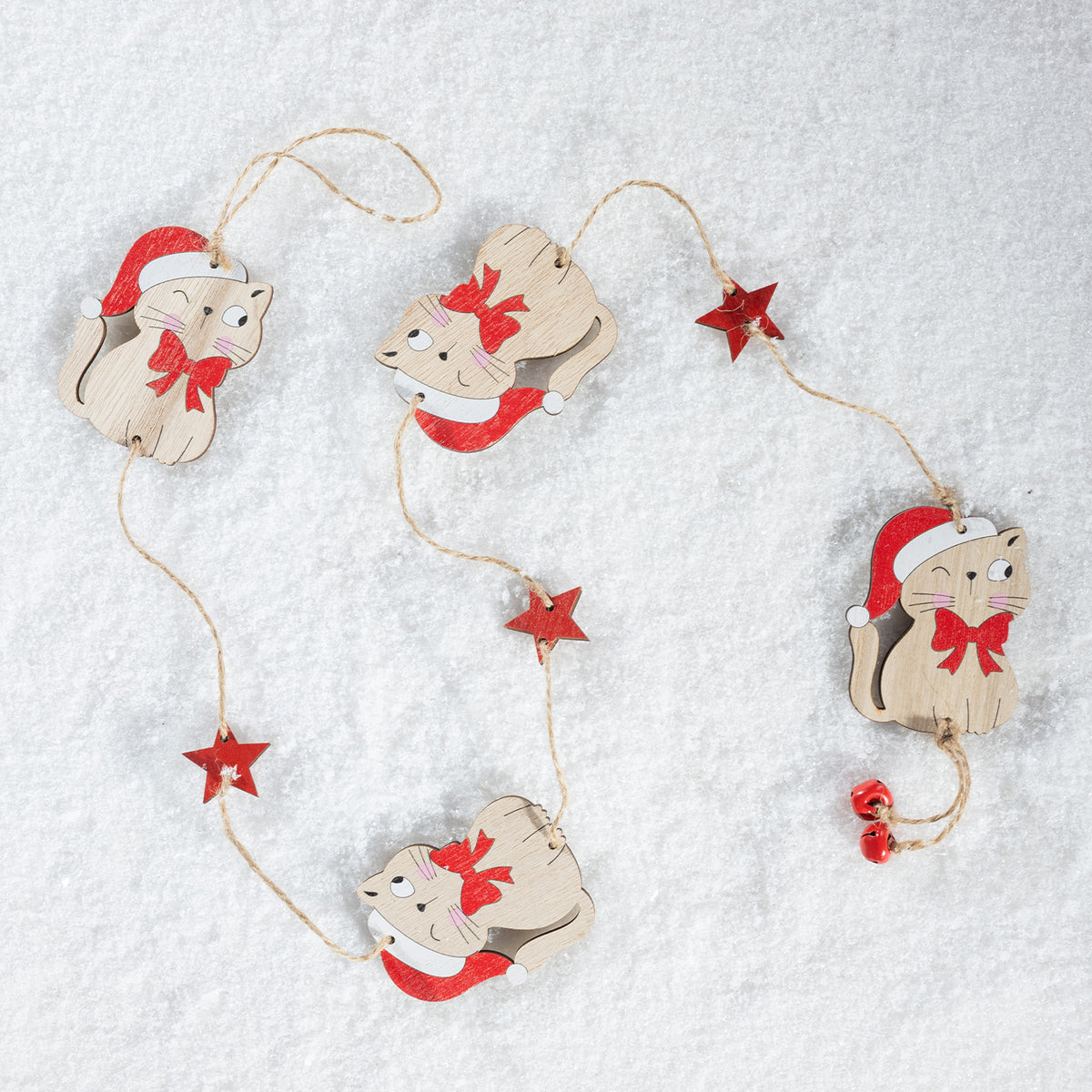 A Christmas garland featuring four wooden cat ornaments wearing red Santa hats and red bows, connected by a string with small red star accents, laid out on a white textured surface.