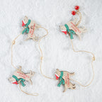 Four wooden Christmas ornament poodles wearing green and red striped scarves, arranged on a white textured background with jute hanging strings and red hanging beads.