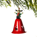 A Christmas ornament shaped like a red bell with a small reindeer figurine perched on top, hanging from a green pine branch against a white background.