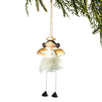 A hanging fairy Christmas ornament with a white fluffy dress, gold wings, a small gold crown, and long thin legs, suspended against a white background with pine branches at the top.