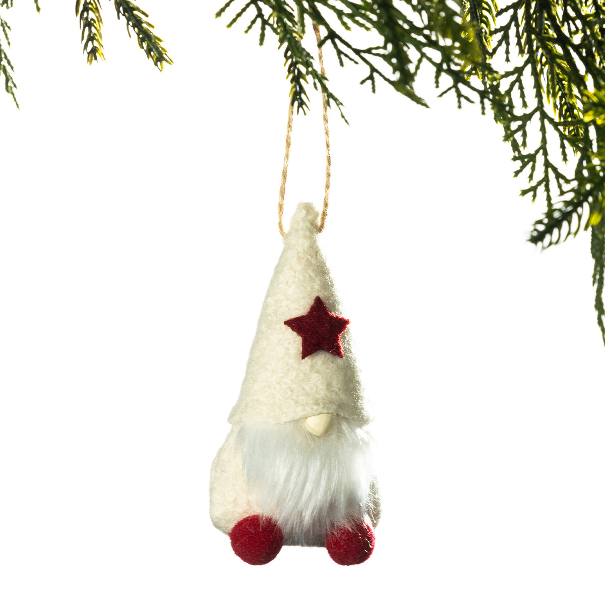 A small felt Christmas gnome ornament hanging from a string, with a cream hat, white beard, red star, and red feet, shown against a white background with pine branches at the top.