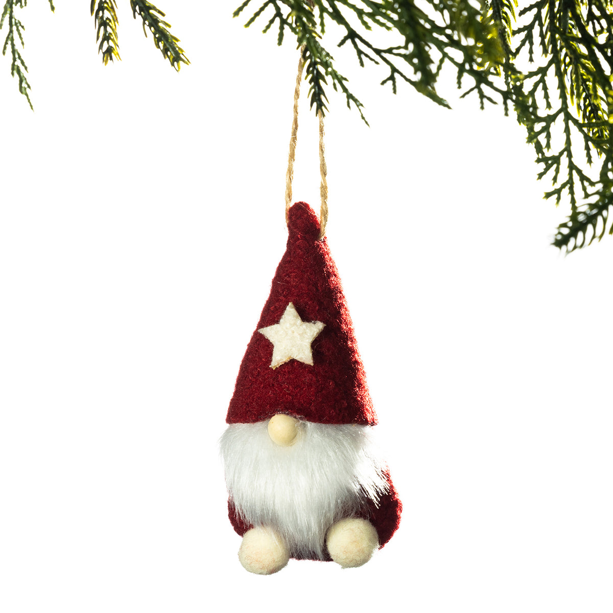 A small felt Christmas gnome ornament hanging from a tree branch against a white background. The gnome has a red pointed hat with a cream star, a white fluffy beard, and cream-colored feet.