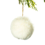 A fluffy cream faux-fur hanging ornament or pom-pom decoration suspended by a natural jute string from green pine branches, isolated on a white background.