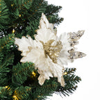 A white artificial poinsettia-style Christmas ornament with glittery gold accents and rhinestone-embellished wings, displayed on a green Christmas tree branch against a white background.