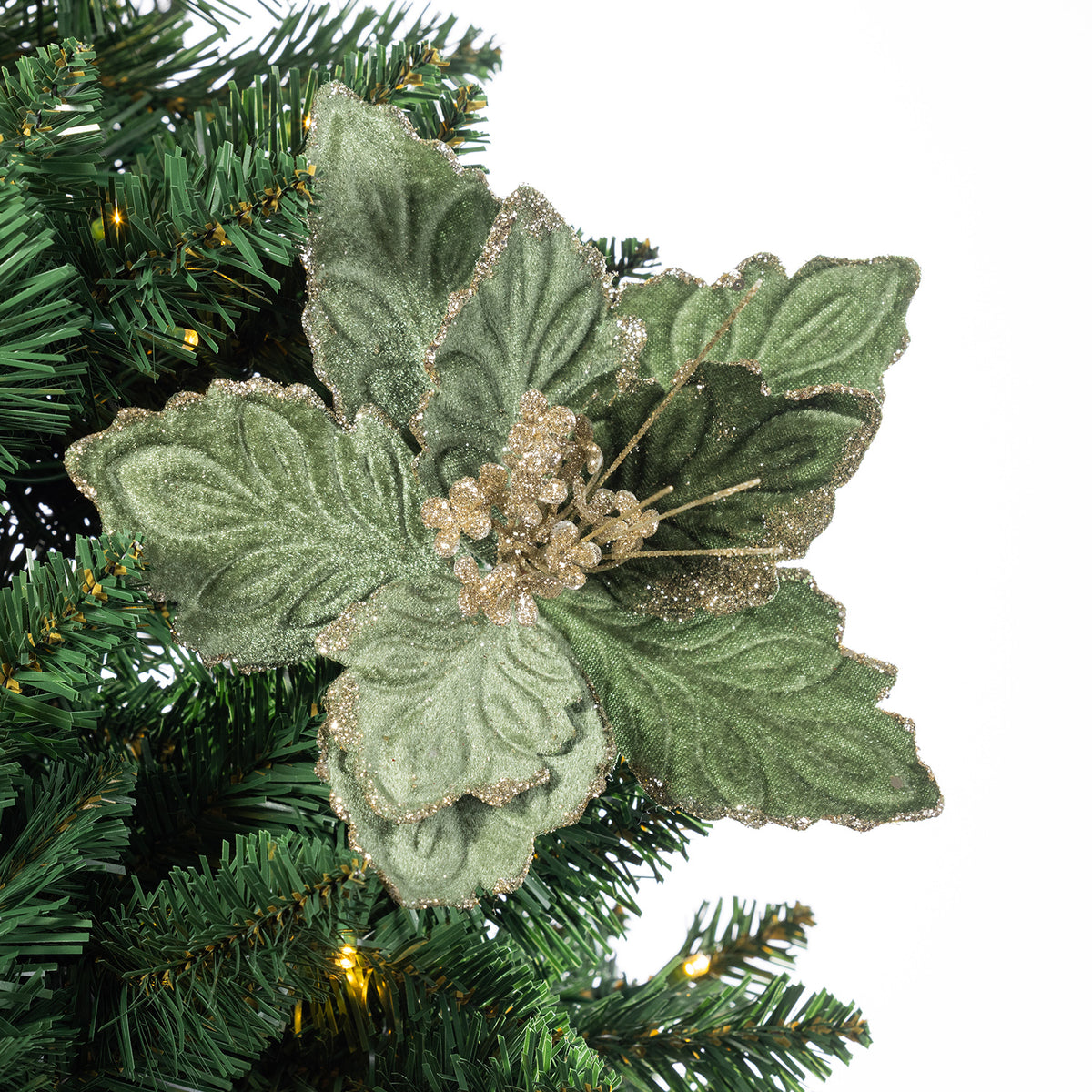 A green artificial poinsettia-style Christmas tree ornament with textured leaves and glittery gold berry accents, shown attached to a green artificial Christmas tree branch against a white background.