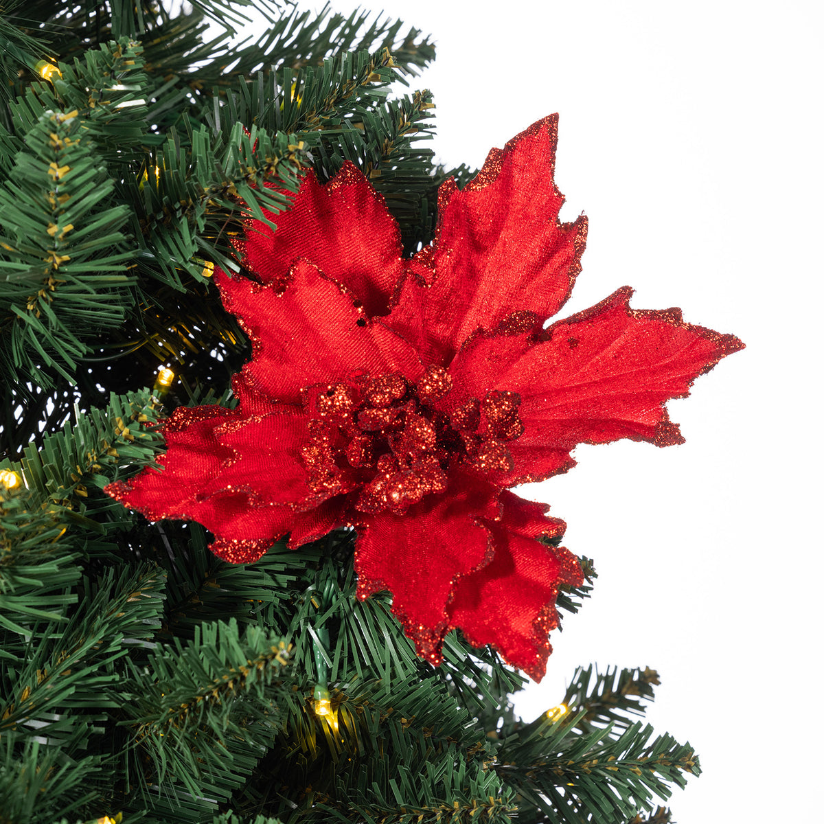 A bright red artificial poinsettia flower ornament with glittery edges, displayed on a green artificial Christmas tree branch against a white background.