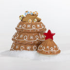 A Christmas-themed ceramic container shaped like a gingerbread tree, with a matching lid placed in front. The tree has brown glazed layers decorated with white icing-style snowflakes and swirls, small multicolored candy accents, and a red star on top.