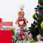 A gingerbread figurine sitting on Christmas presents and next to a Christmas Tree.