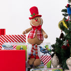 A gingerbread figurine sitting on Christmas presents and next to a Christmas Tree.