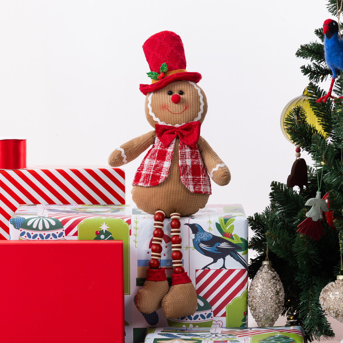 A gingerbread figurine sitting on Christmas presents and next to a Christmas Tree.