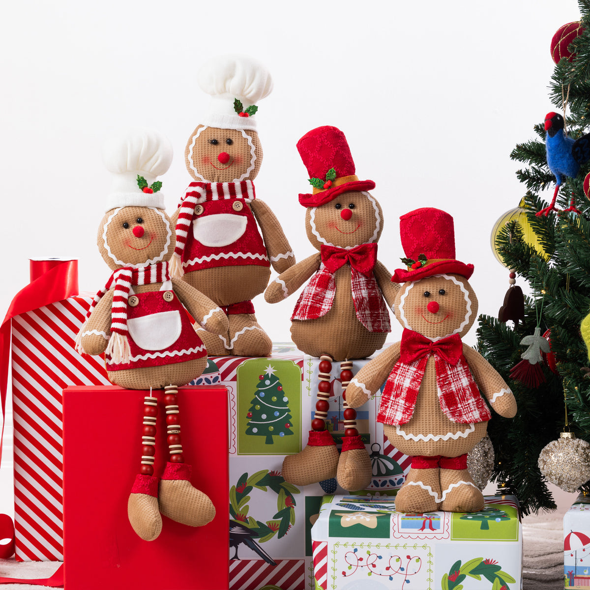 Four Christmas gingerbread figurines in different heights and outfits, styled on top of wrapped gifts next to a decorated Christmas tree.