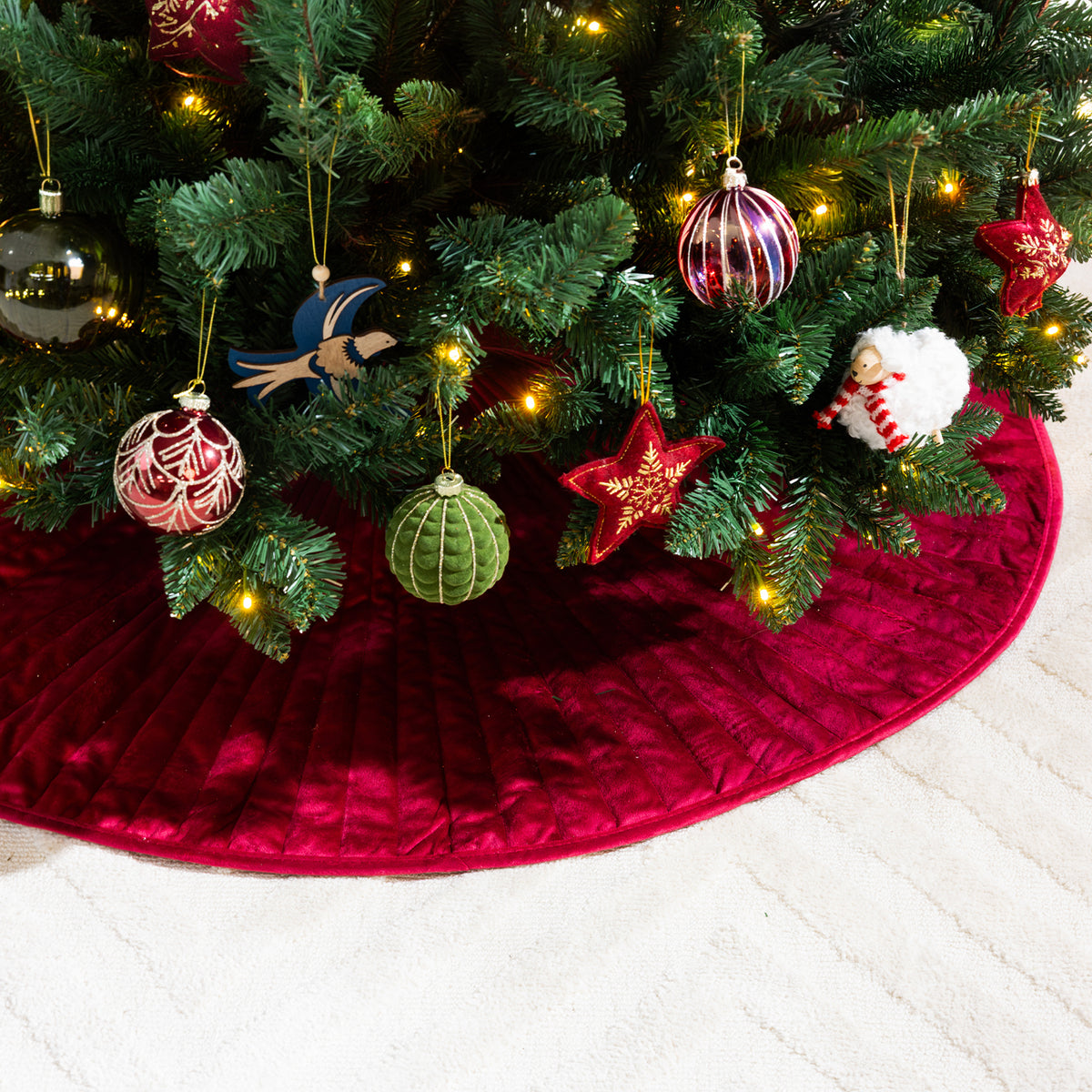 Close-up of the red channel velvet Christmas tree skirt, showcasing its plush texture and stitched detailing beneath festive Christmas decorations.