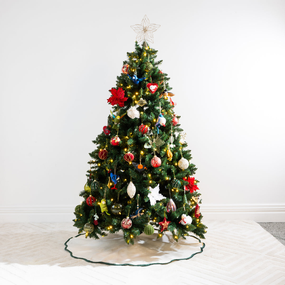 Christmas Wishes Scallop Linen Look Tree Skirt in Natural with dark green scalloped edging, displayed beneath a decorated Christmas tree.