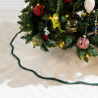 Detailed view of the natural linen-look Christmas tree skirt featuring dark green scalloped edging beneath decorated Christmas tree branches.