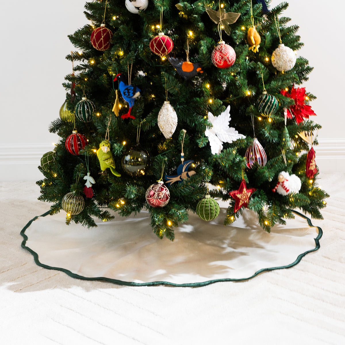 Close-up of the natural linen-look Christmas tree skirt with dark green scalloped edging, surrounded by festive decorations and warm Christmas lights.