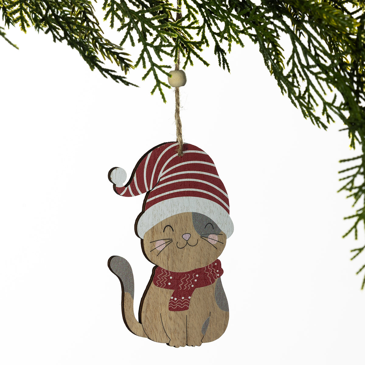 A wooden cat Christmas ornament hanging from a pine branch. The ornament features a smiling cat with a half-wood, half-gray finish, wearing a red and white striped Santa hat and a red patterned scarf.