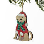 A wooden Christmas ornament shaped like a sitting dog wearing a red sweater, green striped scarf, and red Santa hat, hanging from a jute string under pine branches against a white background.