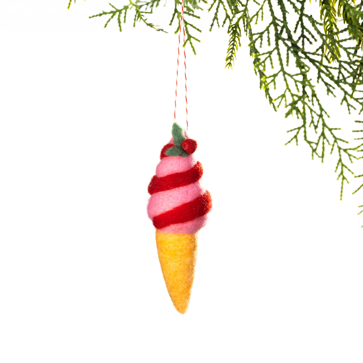 A pink felt strawberry ice cream decoration featuring a red spiral swirl, yellow cone and green holly detailing, hanging from a Christmas tree branch against a white background.