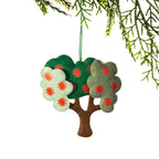 A felt pōhutukawa tree Christmas decoration featuring layered green foliage in different shades, bright red flower details and a brown tree trunk, hanging from a Christmas tree branch against a white background.