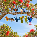 A set of felt nz bird ornaments hanging from a tree branch outdoors against a blue sky with red pohutukawa flowers. 