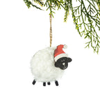 A fluffy white sheep Christmas decoration featuring soft curly wool, a black wooden face, black legs and a red Santa hat, hanging from a Christmas tree branch against a white background.