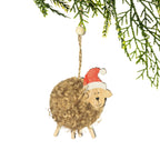 A fluffy brown sheep Christmas decoration featuring natural curly wool, a smiling wooden face, wooden legs and a red Santa hat, hanging from a Christmas tree branch against a white background.