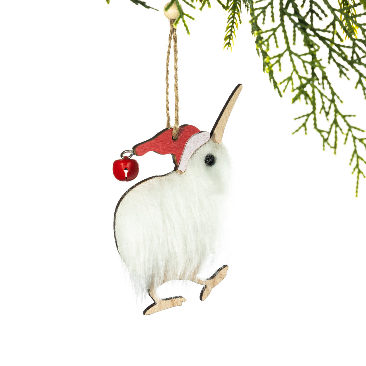 A fluffy white kiwi Christmas decoration featuring soft feather-like fur, a long wooden beak, wooden feet and a red Santa hat with a small bell, hanging from a Christmas tree branch against a white background.