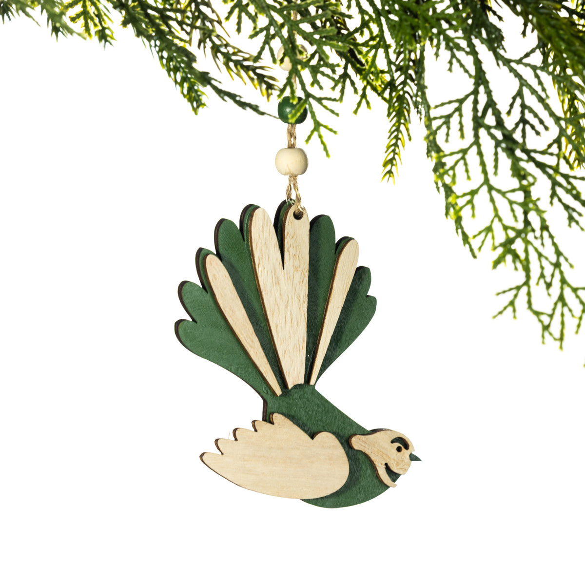 A wooden pīwakawaka Christmas decoration featuring a green and natural wood colourway, layered wings and a distinctive fan-shaped tail, hanging from a Christmas tree branch against a white background.