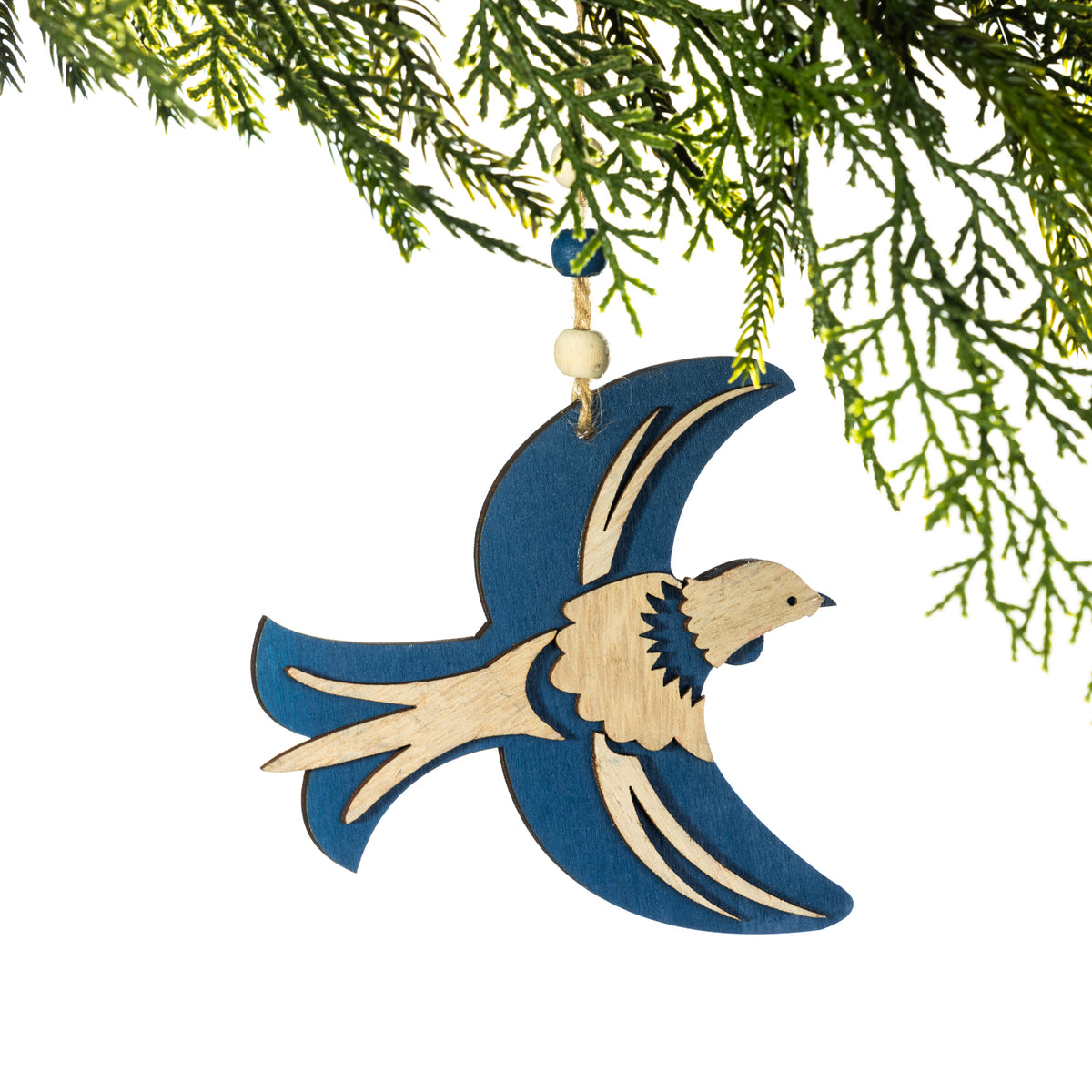 A wooden tūī Christmas decoration featuring a rich teal and natural wood design, layered wings and a long pointed tail, hanging from a Christmas tree branch against a white background.