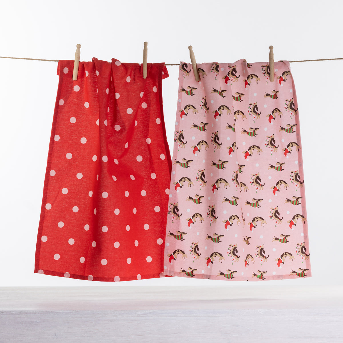 Christmas Wishes Dashing Dachshund tea towel 2 pack with red polka dot tea towel and pink festive dachshund print tea towel hanging on a line.