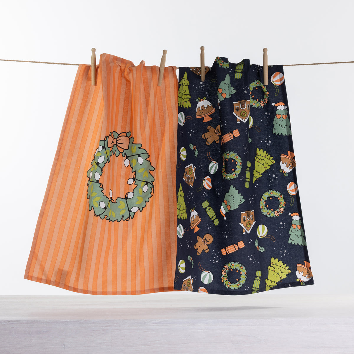 Christmas Wishes Festive Icons tea towel 2 pack with orange wreath design and navy Christmas icon print hanging on a line.