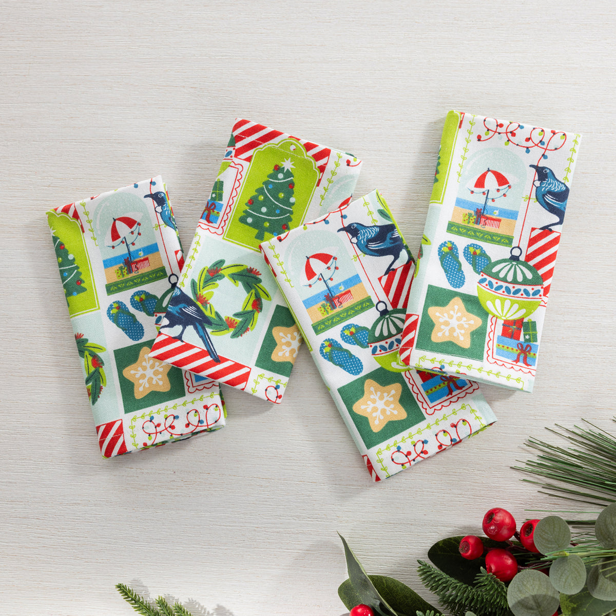 Christmas Wishes Kiwi Christmas 4 pack napkins arranged flat, featuring the colourful festive print with trees, wreaths, birds, ornaments and gifts.