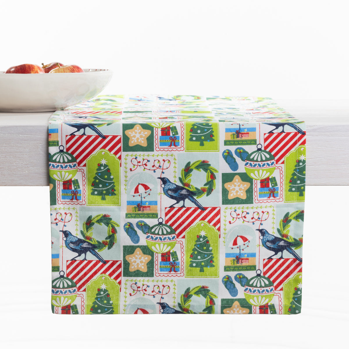 Christmas Wishes Kiwi Christmas table runner styled across a white table, featuring Christmas trees, native birds, wreaths, ornaments and gifts.